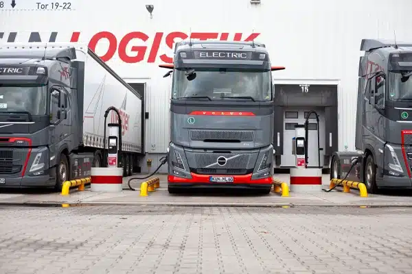 Elektrischer Volvo‑Lkw an einer Schnellladestation vor einer Logistikhalle im Rahmen von Werks- und Shuttleverkehren
