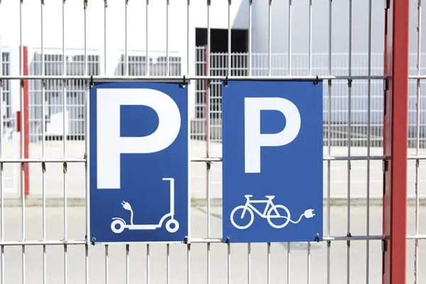 Parkplatzschilder für E-Scooter und Fahrräder am Zaun